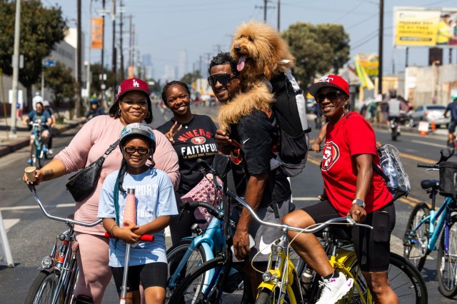 Multigenerational African-American family of five people and one dog in a backpack post with their bikes.